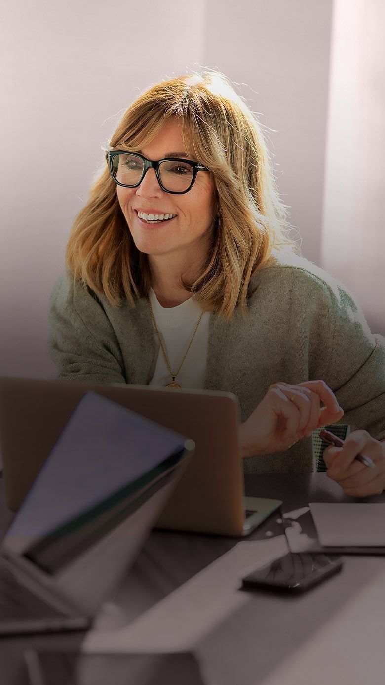 Main hero image for RHR’s About Us section featuring a woman smiling during a collaborative workplace meeting while seated at a laptop in a bright modern office, representing leadership, partnership, and professional connection.