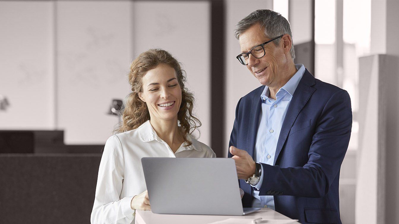 Image featuring two professionals reviewing information together on a laptop in a modern office, representing collaboration, mentoring, leadership development, and teamwork as a career at RHR.