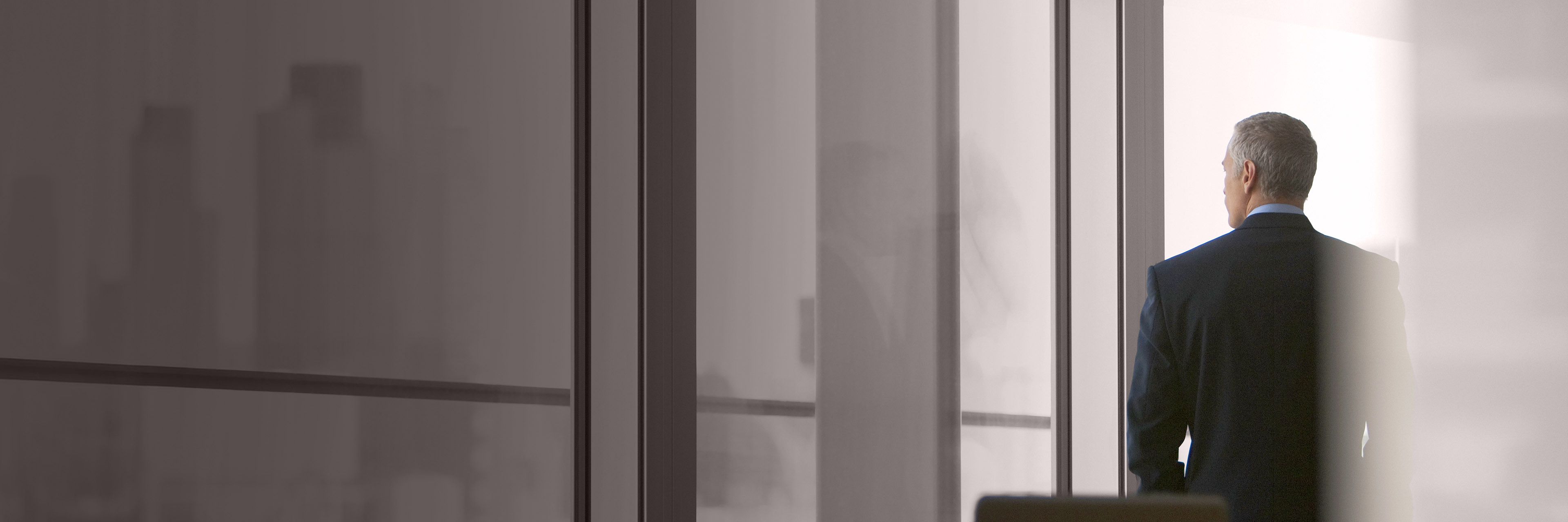 Executive standing in a conference room looking out a window, representing leadership, strategic thinking, and executive decision-making.