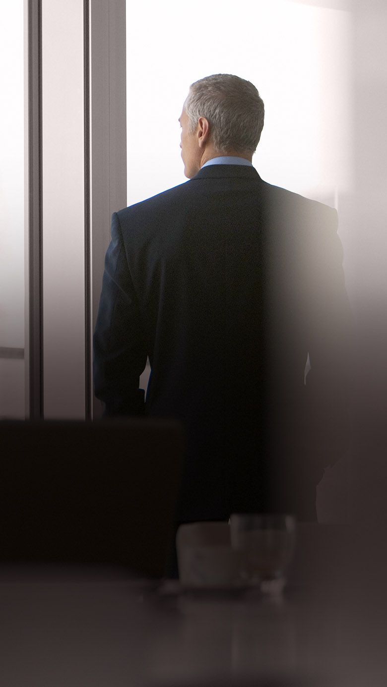 Executive standing in a conference room looking out a window, representing leadership, strategic thinking, and executive decision-making.
