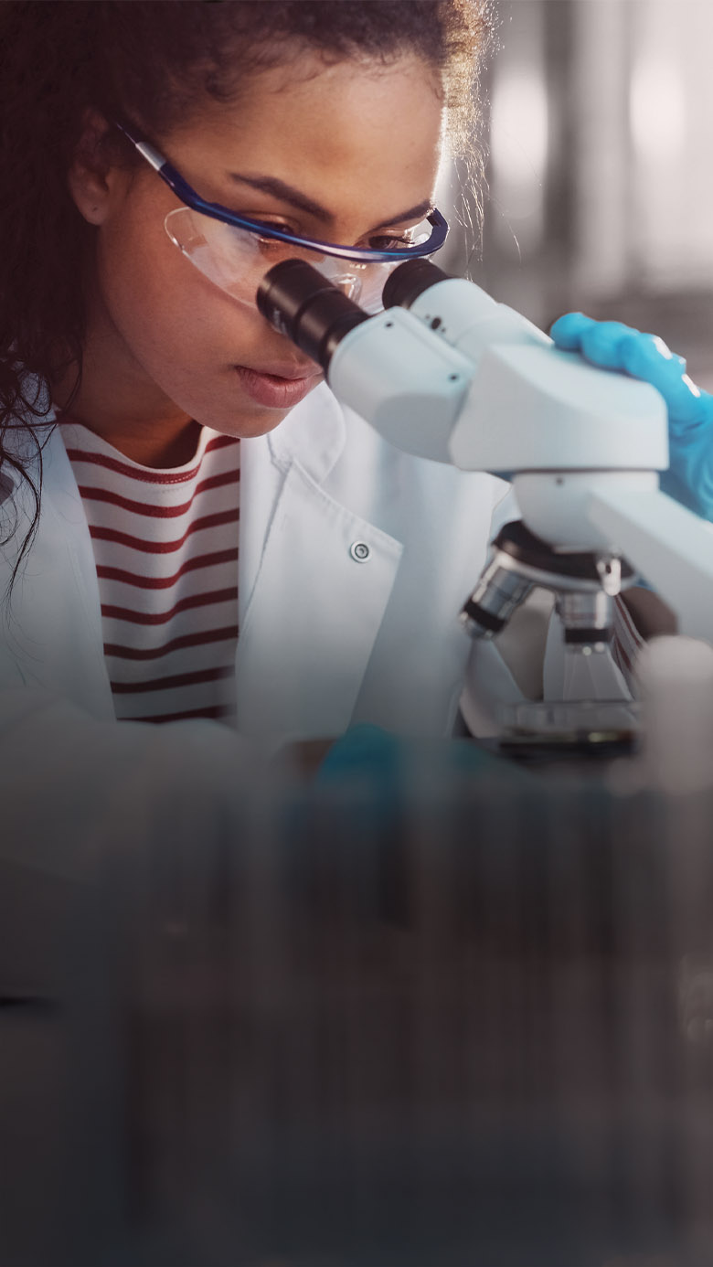 Research professional looking through a microscope, representing leadership assessment, executive coaching, and onboarding and transition support.