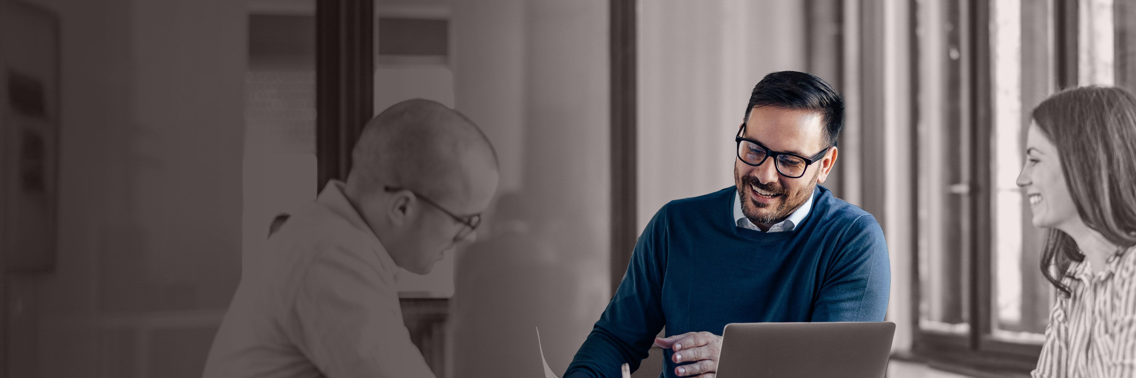 Three professionals collaborating at a conference table with a laptop, representing executive coaching, leadership development, and business partnership.