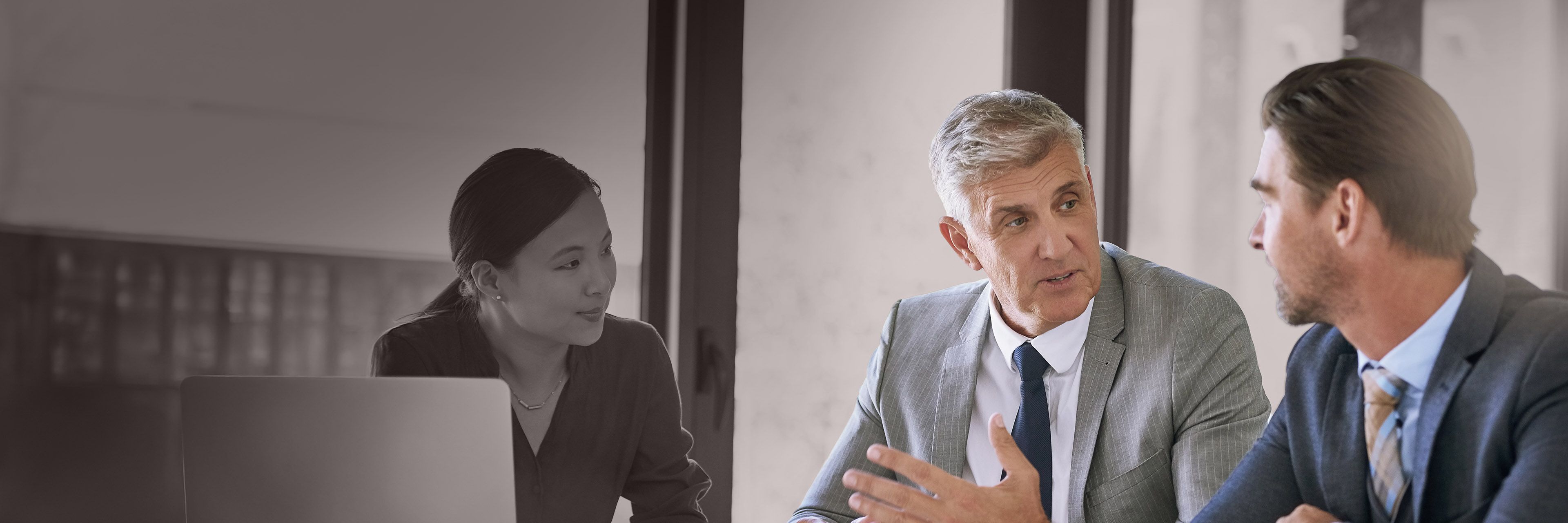 Three executives in discussion during a business meeting, representing executive coaching, strategic leadership, and collaborative decision-making.