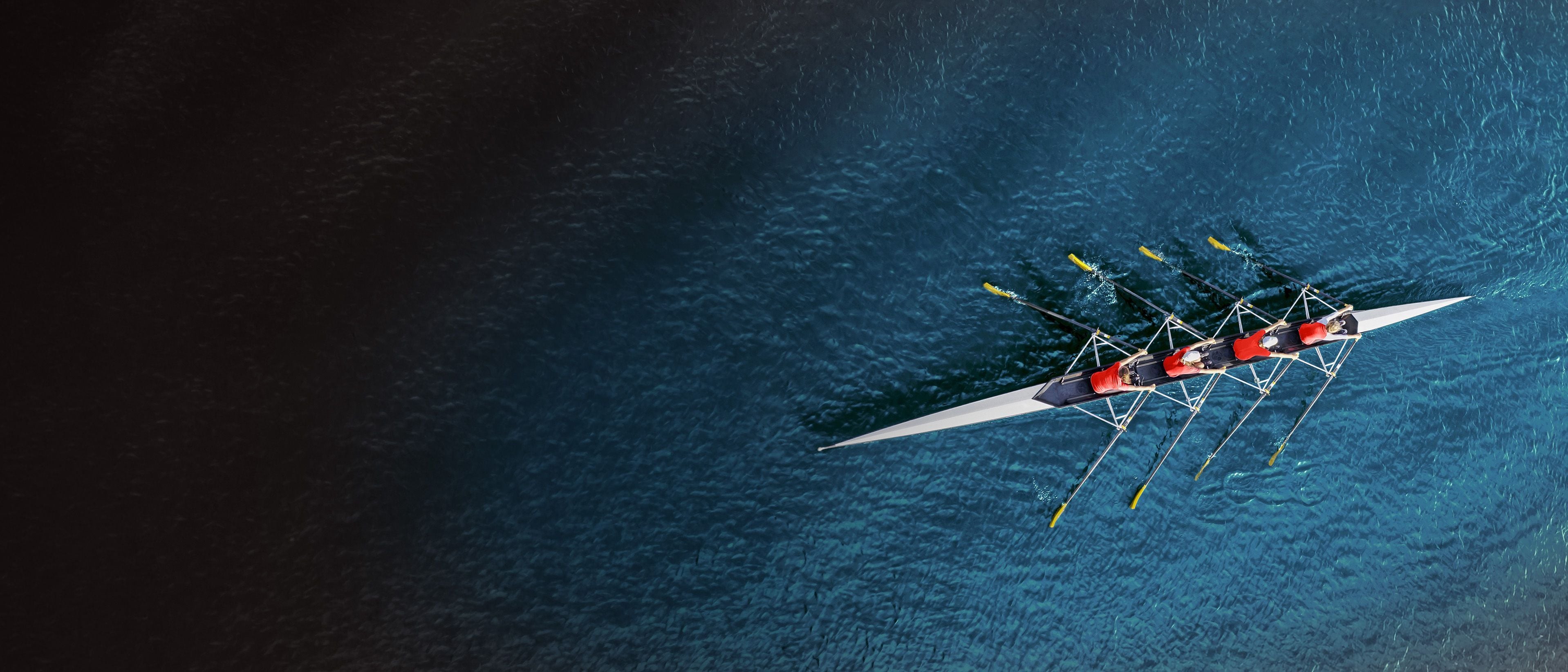 Aerial view of a four-person rowing crew in a racing shell, representing synchronized team leadership and coaching in private equity.