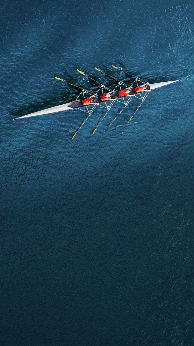 High-angle view of a rowing crew on open water, depicting high-performing team dynamics.