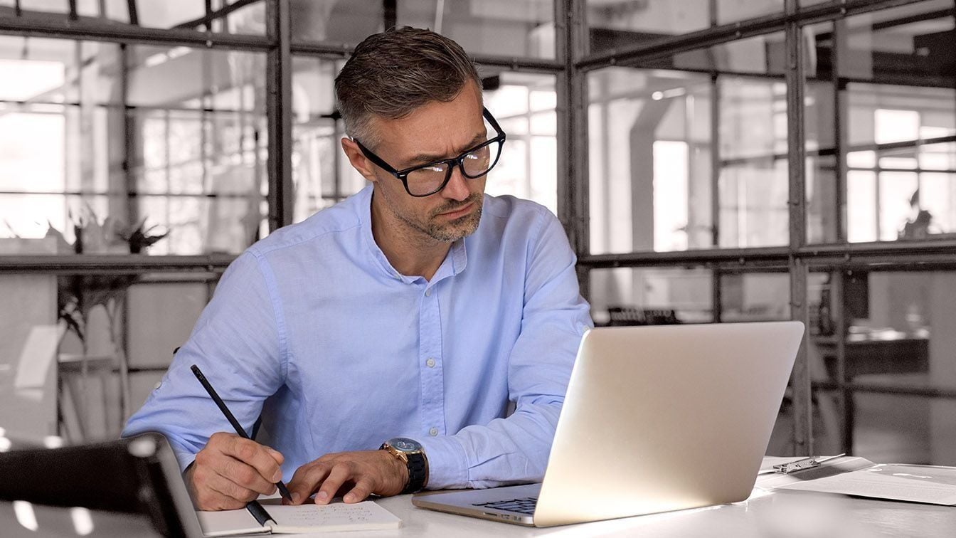 Image of a business executive working at a laptop in a modern office, representing leadership evaluation, strategic analysis, and RHR’s Executive Assessment Solutions.