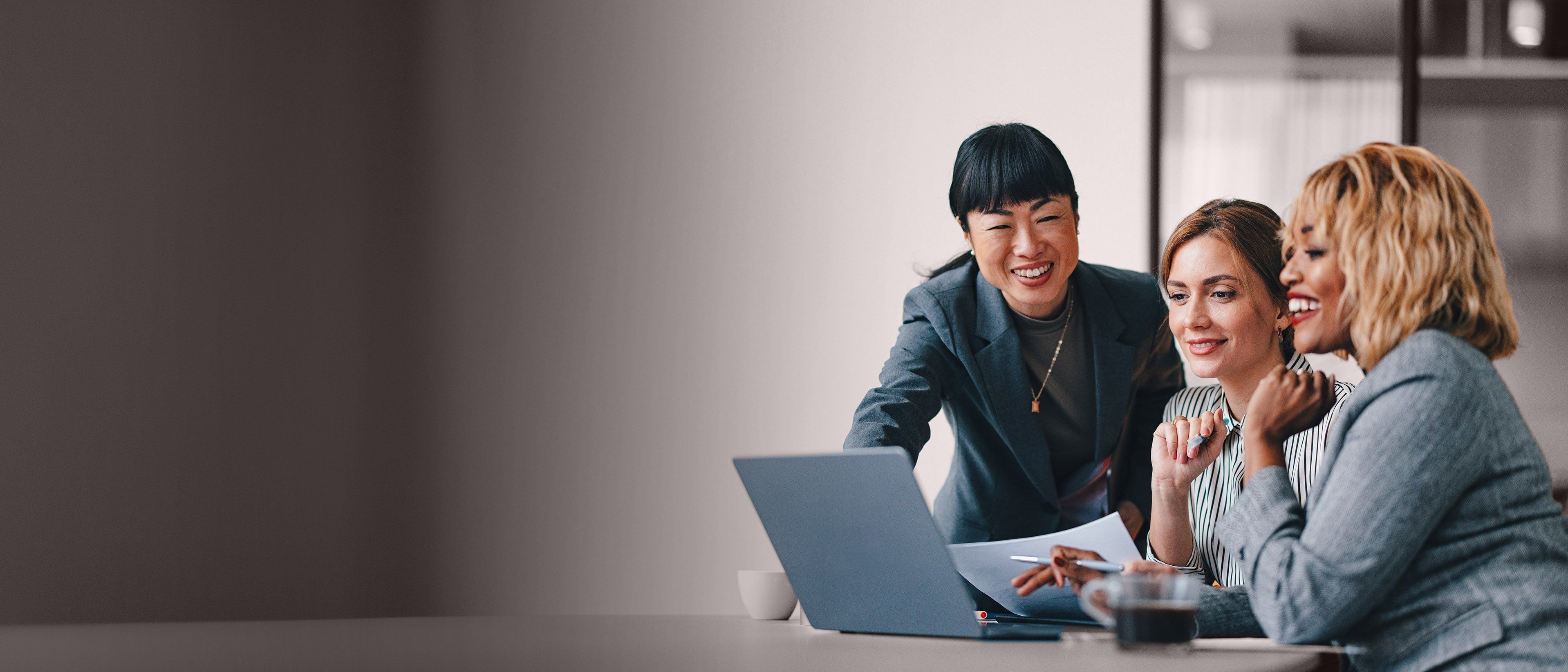 Wide banner image of business professionals collaborating around a laptop, representing workforce insights, talent analytics, and RHR’s People Analytics Solutions.